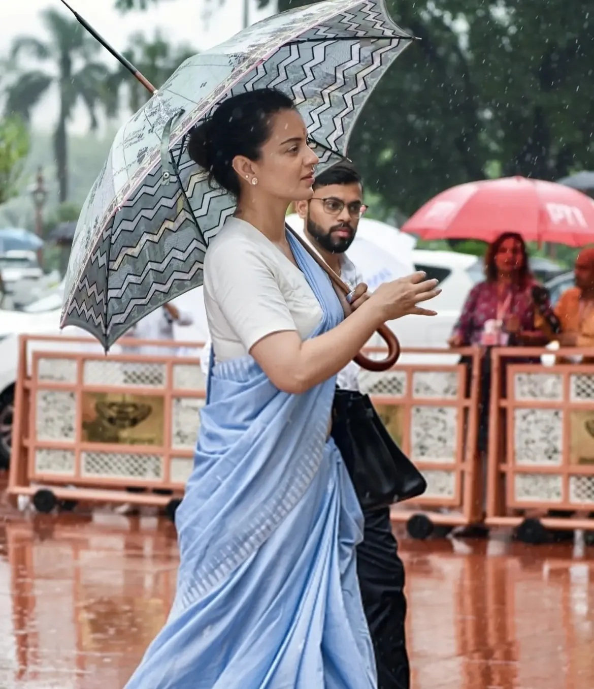एक्ट्रेस और BJP सांसद  दिल्ली में बारिश के दिन हल्के नीले रंग की साड़ी पहने हुए पार्लियामेंट जाते हुए देखी गईं।